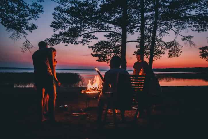 Group of young happy friends sitting by the fire at summer beach