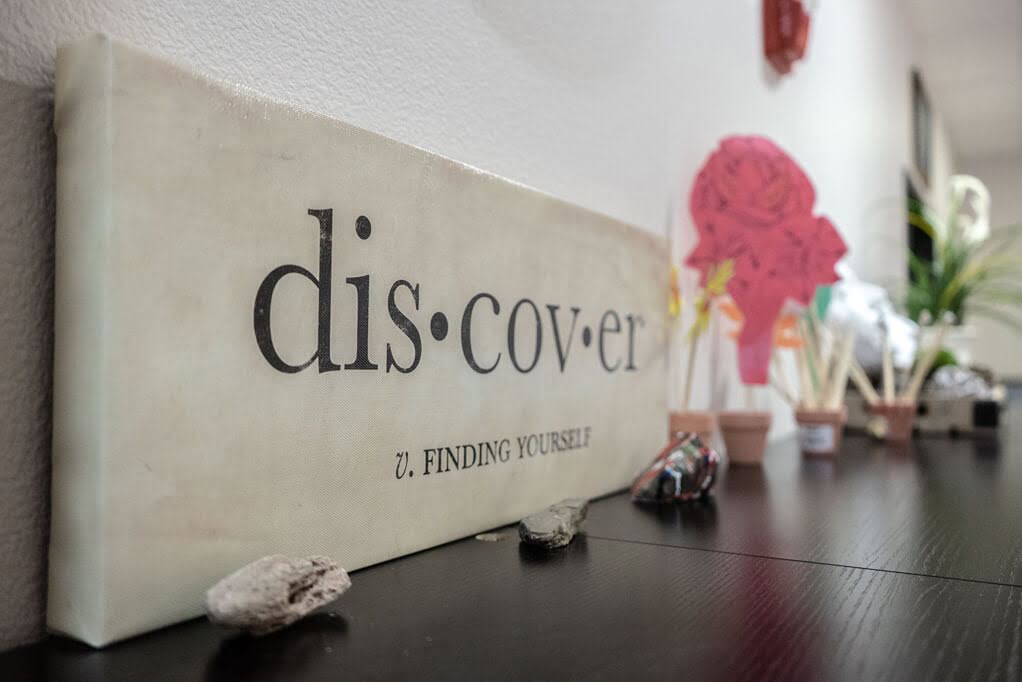 Close up of marble sign with the word Discover and the definition saying 'Finding Yourself' on a credenza with plants